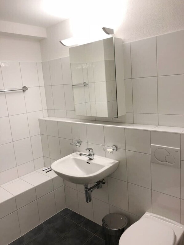 A bathroom with a white sink, a mirror above it, and a toilet. - Centrally located, Spacious Modern Apartment (Zürich)