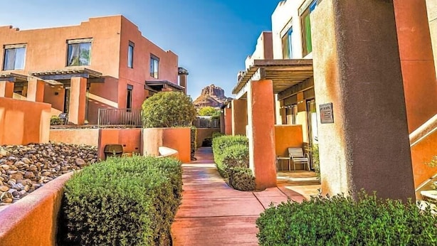 A hotel courtyard with a central pathway, surrounded by buildings with balconies and a mountain view in the background.