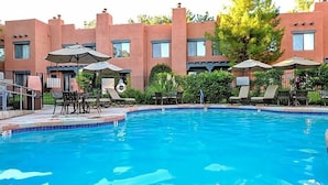 A swimming pool with lounge chairs and umbrellas, surrounded by a building with a terracotta facade.