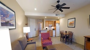 A living room with a sofa, armchair, ottoman, dining table, and chairs. A ceiling fan is visible.