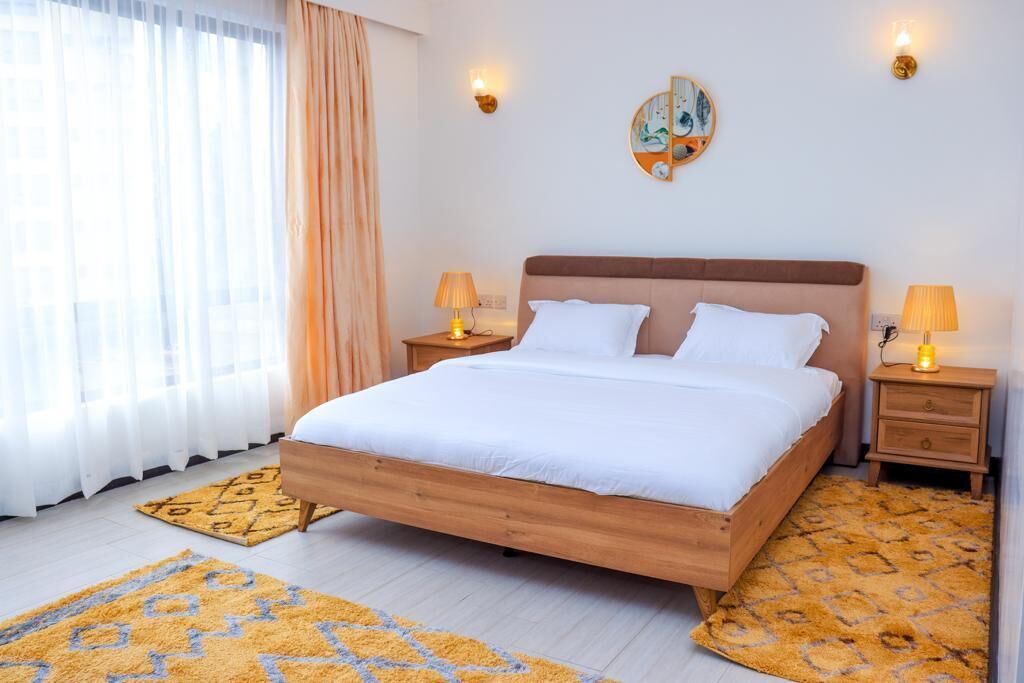 A bedroom with a wooden bed, two bedside tables with lamps, a wall art piece, and a patterned rug.