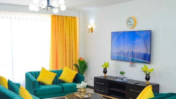 Un salon moderne avec des canapés de couleur turquoise, une table basse et un téléviseur fixé au mur.