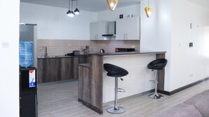 Une cuisine moderne dotée d’un îlot central, de tabourets de bar, de luminaires suspendus et d’un distributeur d’eau.