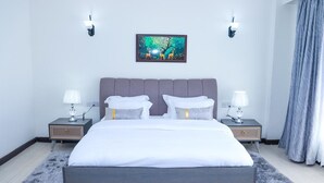 Une chambre moderne avec un grand lit, deux tables de chevet avec des lampes, une œuvre d’art accrochée au mur et un tapis gris.
