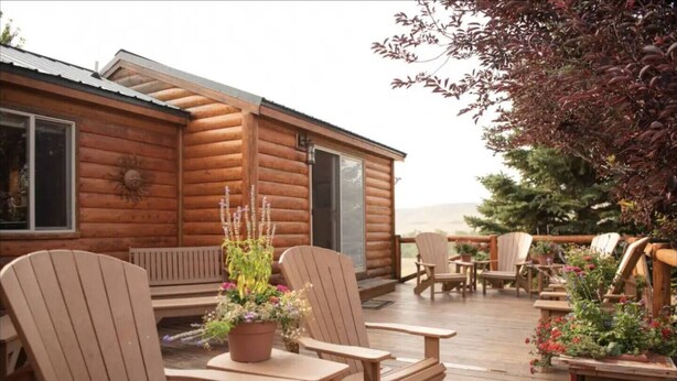 Eine Holzhütte mit einer Terrasse, Sitzgelegenheiten im Freien und einem großen Fenster.