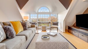 A modern living room with a high ceiling, a large window, a sofa, a coffee table, and a flat-screen TV.