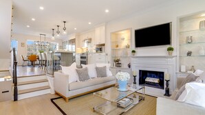 A modern living room with a fireplace, a dining area, and a kitchen.