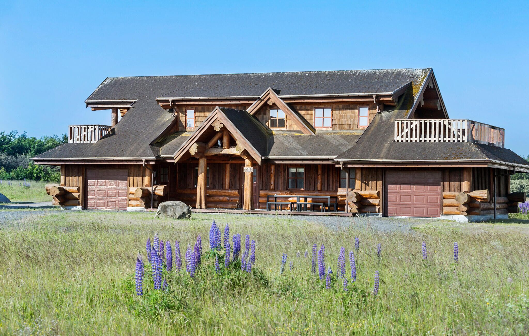 A large log cabin with a front porch, multiple windows, and a covered deck.