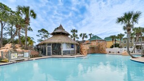 A swimming pool with a thatched-roof structure, palm trees, and a rocky landscape. - Family-Friendly Pensacola Home < 1 Mi to Beach! (Pensacola)