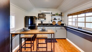 Una cucina compatta con un tavolo di legno, due sgabelli, un forno a microonde e un frigorifero.
