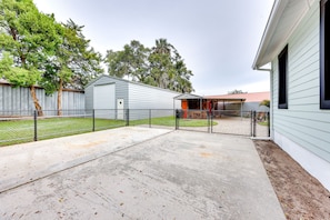 A backyard with a concrete patio, a fenced area, and a building with a red roof.