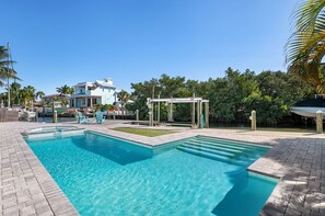 Een zwembad met een pergola, ligbedden en een uitzicht op een groot huis op de achtergrond.