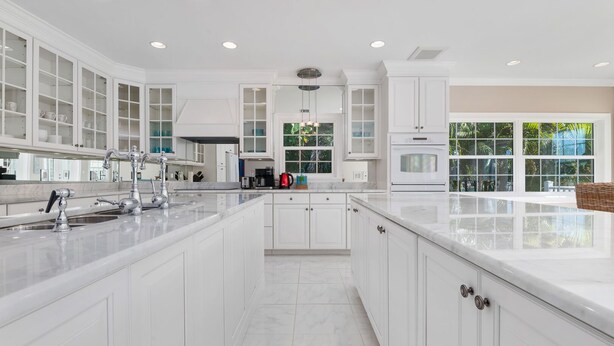 A spacious kitchen with white cabinetry, a large island, and a view of greenery outside.
