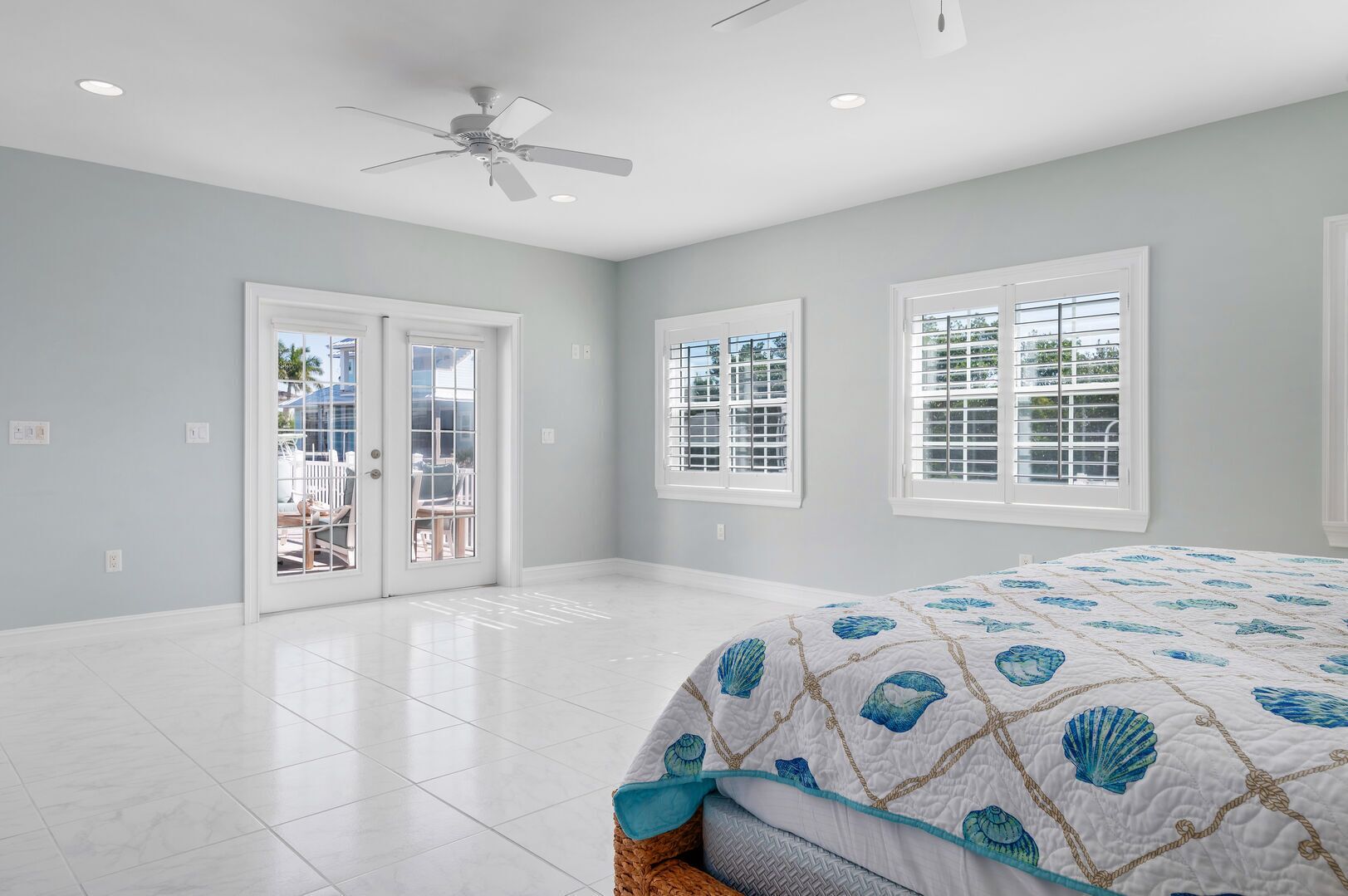A spacious bedroom with a large bed, a ceiling fan, and two windows with blinds.