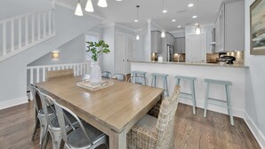 A dining area with a wooden table, metal chairs, and light blue bar stools. There is a white vase with a plant on the table.