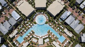 An aerial view of a hotel with a central swimming pool surrounded by lounge areas and palm trees.