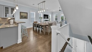 A spacious kitchen with a dining area, wooden flooring, and a white staircase.