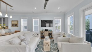 A spacious living room with a large sofa set, a coffee table, and a TV mounted on the wall.
