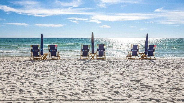 A beach with three rows of beach chairs and umbrellas, facing the ocean.