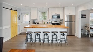 A modern kitchen with white cabinets, a wooden island with bar stools, stainless steel appliances, and a yellow door. - 2 Incredible Units Equal Double the Amenities! Lazy Mermaid (Folly Beach)