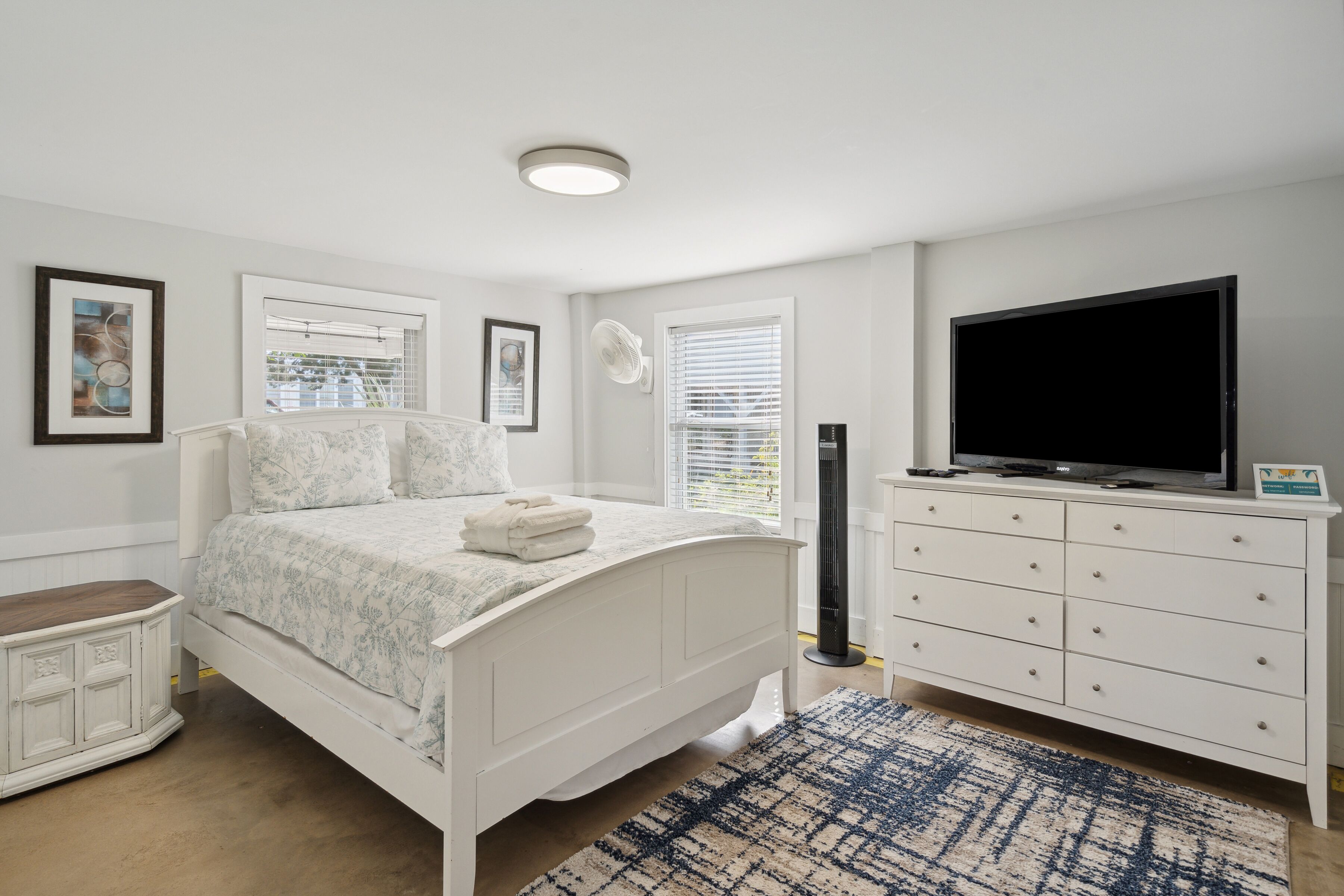 A bedroom with a bed, dresser, TV, and artwork on the walls.