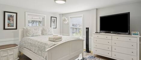 A bedroom with a bed, dresser, TV, and artwork on the walls.