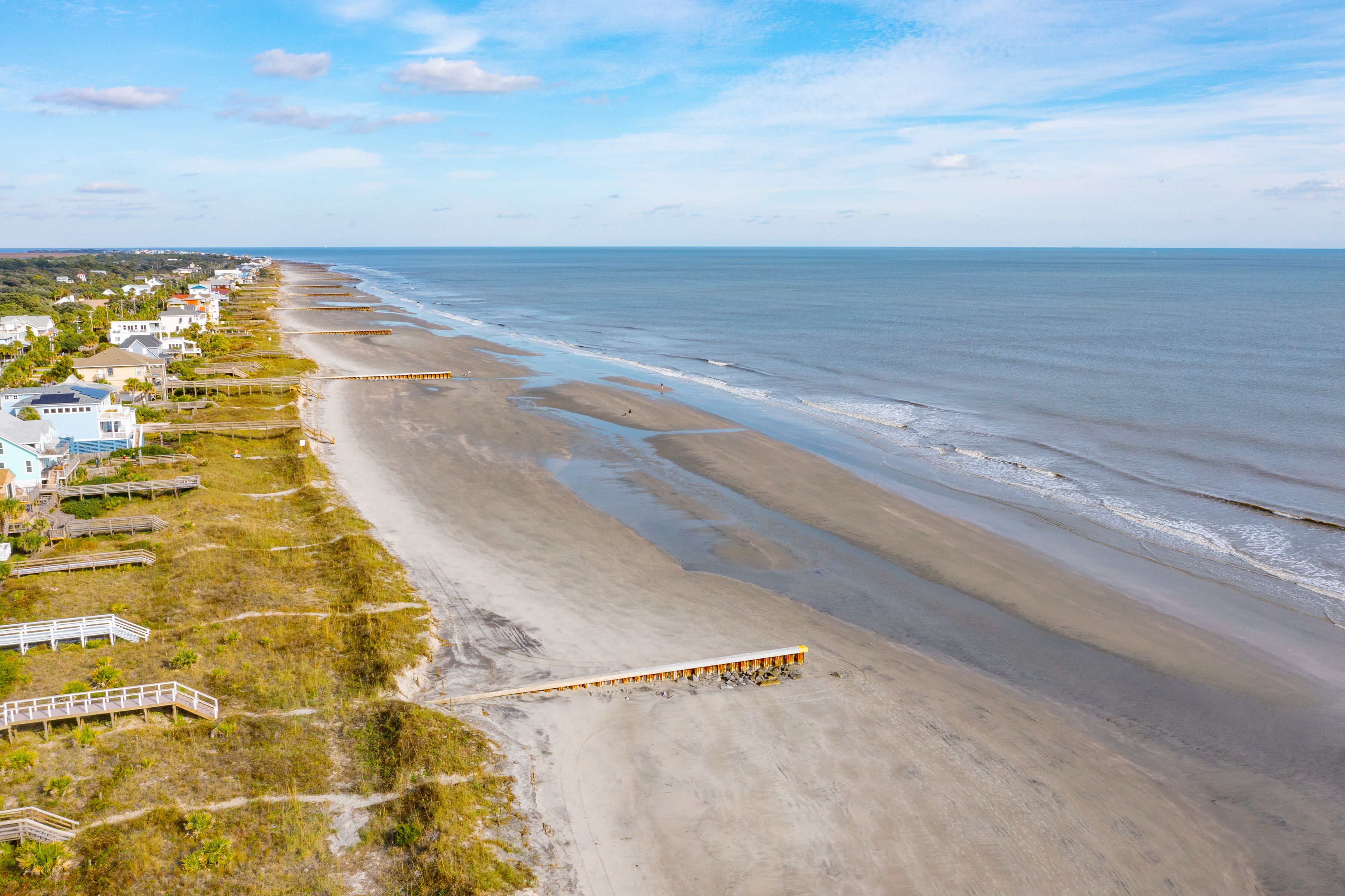 A coastal area with a beach, houses, and a wooden boardwalk.