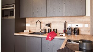 A modern kitchen with dark cabinets, a wooden backsplash, stainless steel appliances, and various kitchen utensils. - Près du Télémixte du Diable | T2 + terrasse & Wifi (Les Deux Alpes)
