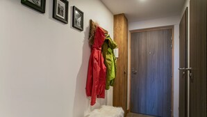 A hallway with a bench, a coat rack with jackets, a wooden door, and framed pictures on the wall. - Près du Télémixte du Diable | T2 + terrasse & Wifi (Les Deux Alpes)