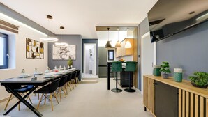 A modern kitchen with a built-in oven, a dining area with a long table and chairs, and a TV mounted on the wall.