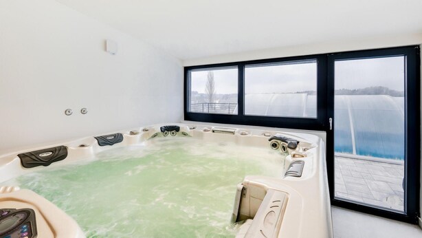 A spa room with a hot tub, a control panel, and a view of a bridge and water body through large windows.
