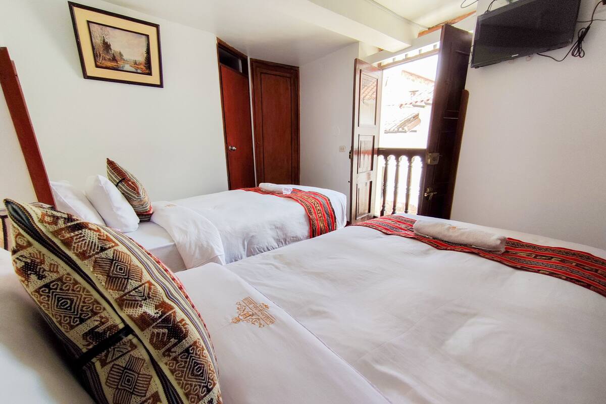 A hotel room with two beds, a painting on the wall, and a TV mounted on the wall.