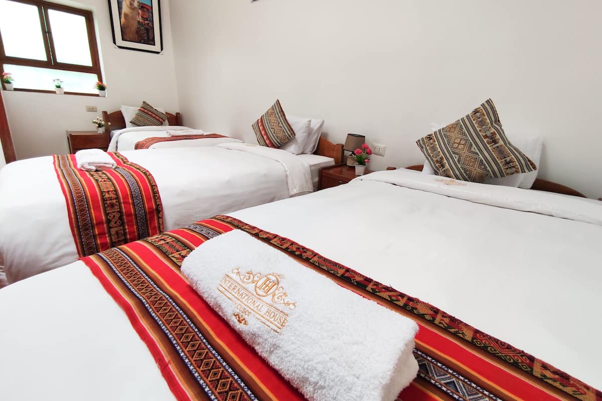 A hotel room with two beds, each with patterned bedspreads and pillows, a nightstand with a lamp, and a window with a view.
