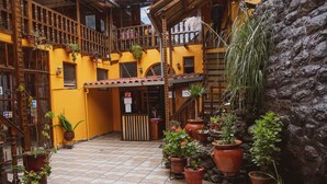 A courtyard with terracotta-tiled floor, potted plants, wooden balconies, and a stone wall. - Hostal International House Cusco (Cusco)