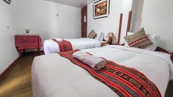 A hotel room with two beds, each with white linens and decorative pillows. There is a small table with a red tablecloth and a vase of flowers.