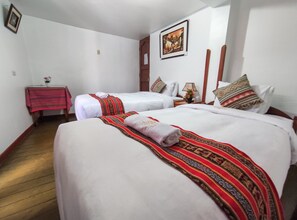 A hotel room with two beds, each with white linens and decorative pillows. There is a small table with a red tablecloth and a vase of flowers. - Hostal International House Cusco (Cusco)