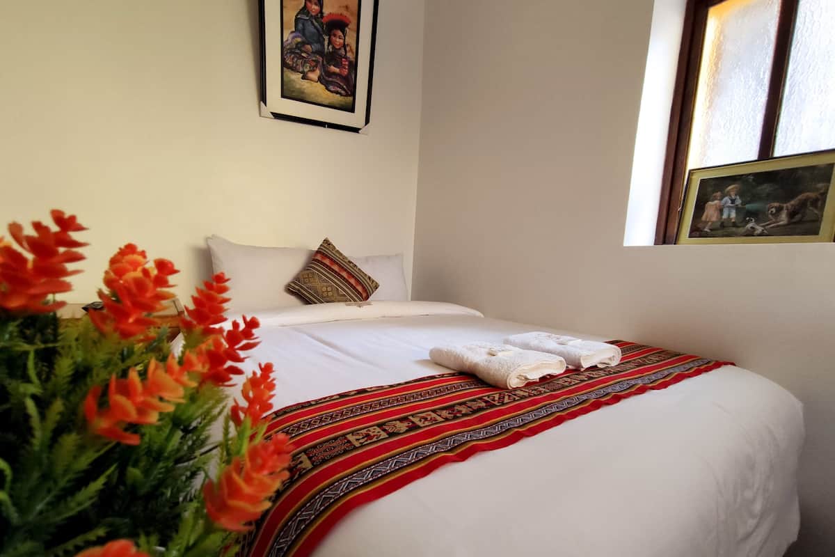 A hotel room with a neatly made bed, a decorative pillow, a framed painting on the wall, and a window with a view.