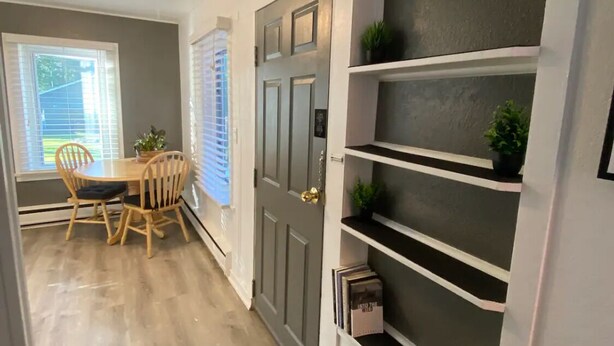 Un pasillo con comedor, una puerta gris y un mueble de almacenamiento con plantas.