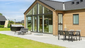 Ein modernes Haus mit einem großen Glasfenster, einer Terrasse mit Gartenmöbeln und einer Holzfassade.