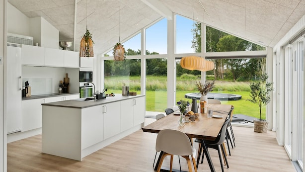 Eine moderne Küche mit weißen Schränken, einem Holzespeisetisch und großen Fenstern mit Blick auf einen Garten.