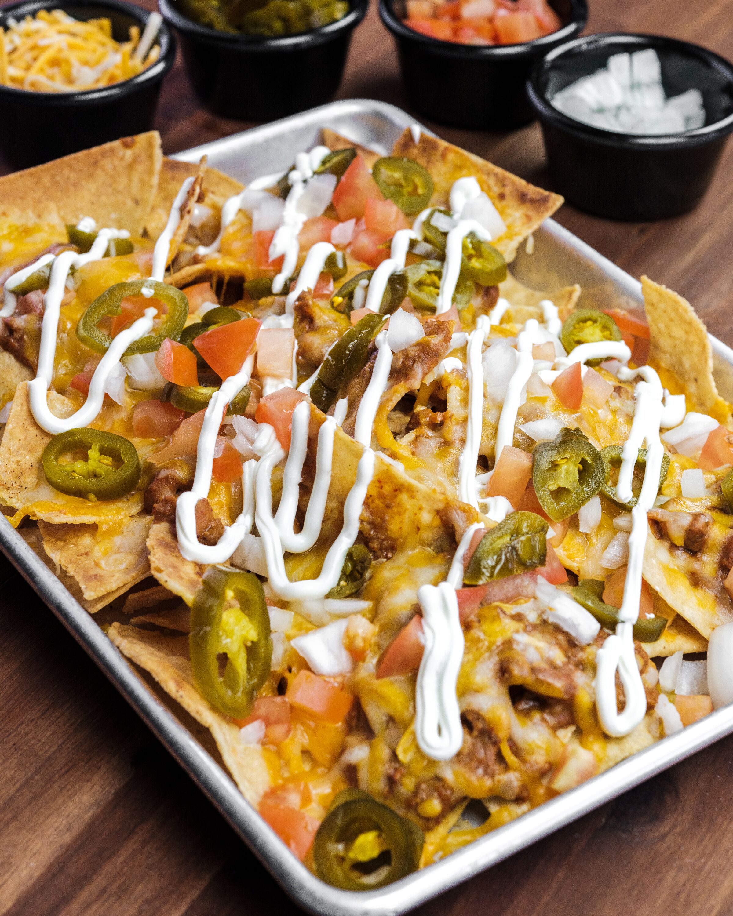 Nachos topped with cheese, jalapeños, tomatoes, and sour cream on a tray.