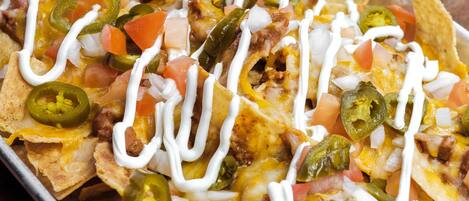 Nachos topped with cheese, jalapeños, tomatoes, and sour cream on a tray.