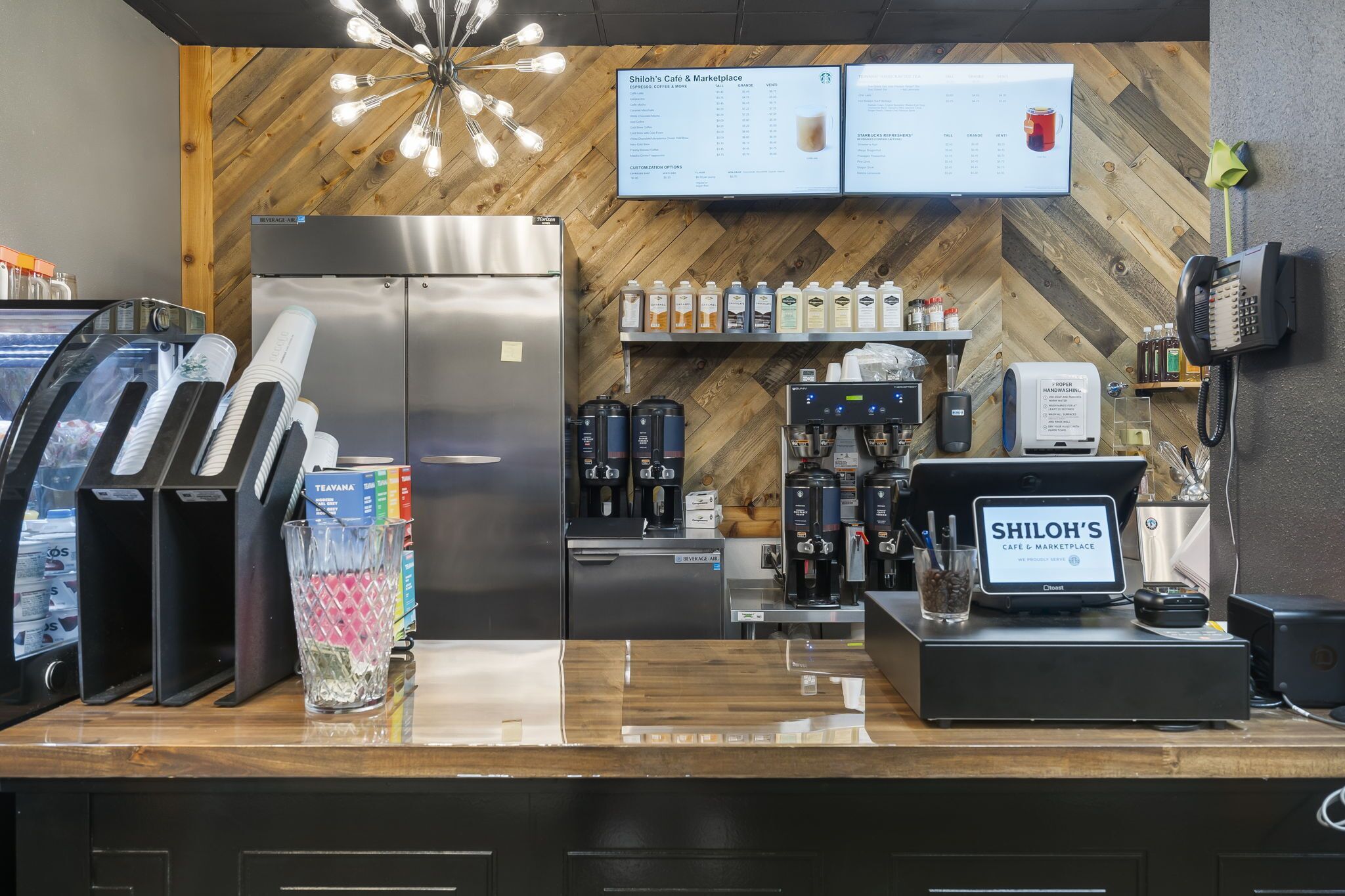 En cafédisk med menutavle, kaffemaskine, køleskab og kasseapparat.