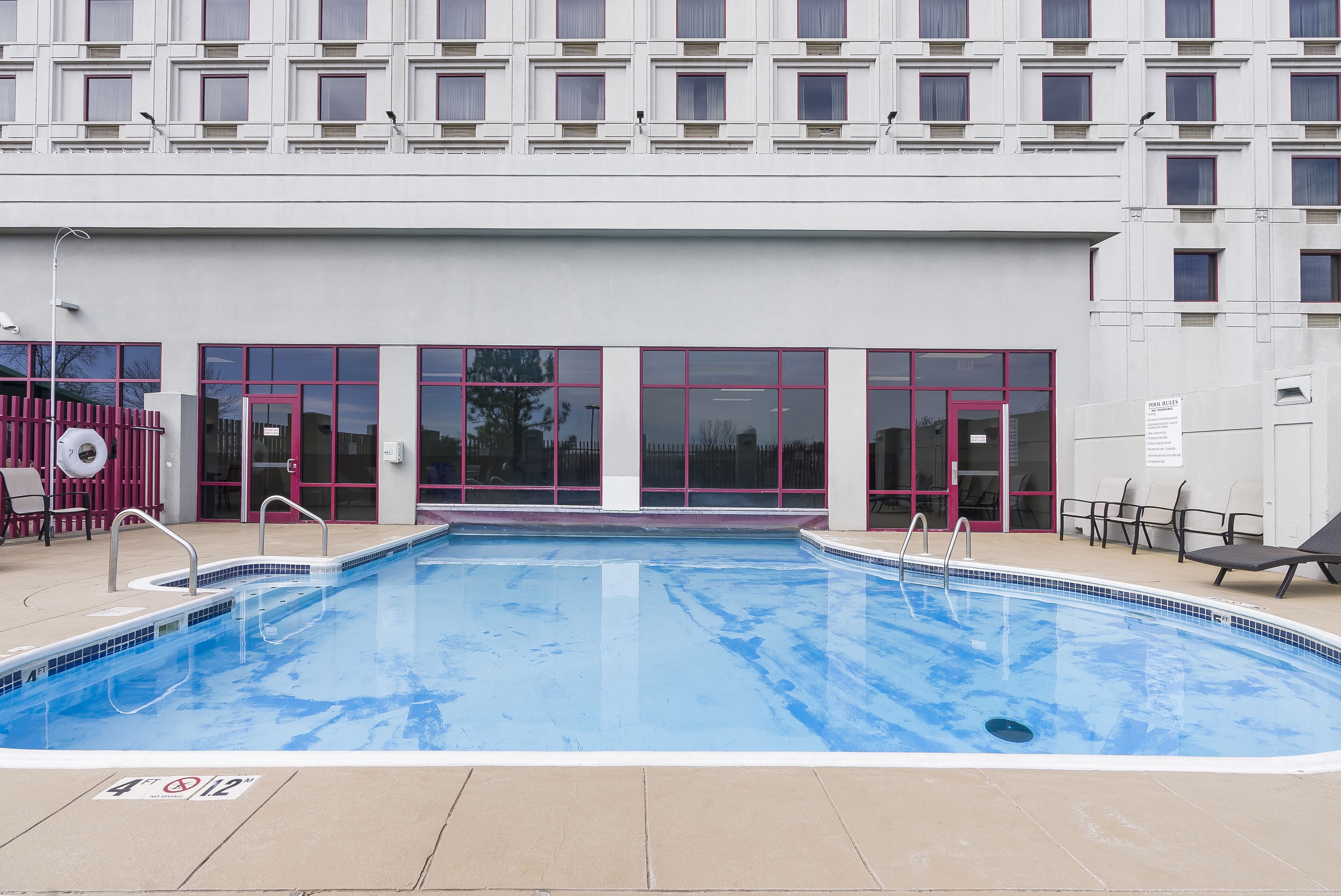 A swimming pool with a tiled edge, adjacent to a building with large windows and a door.