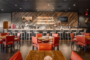 Un restaurant doté d’un bar, de fauteuils en cuir rouge et d’un mur en bois sur lequel est affiché un panneau indiquant « Black Harris ».
