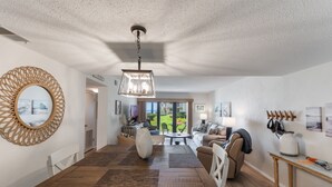 A spacious living area with a dining table, a sofa, and a view of a garden. - Castle Reef 124 - Lovely location on No drive Beach (New Smyrna Beach)