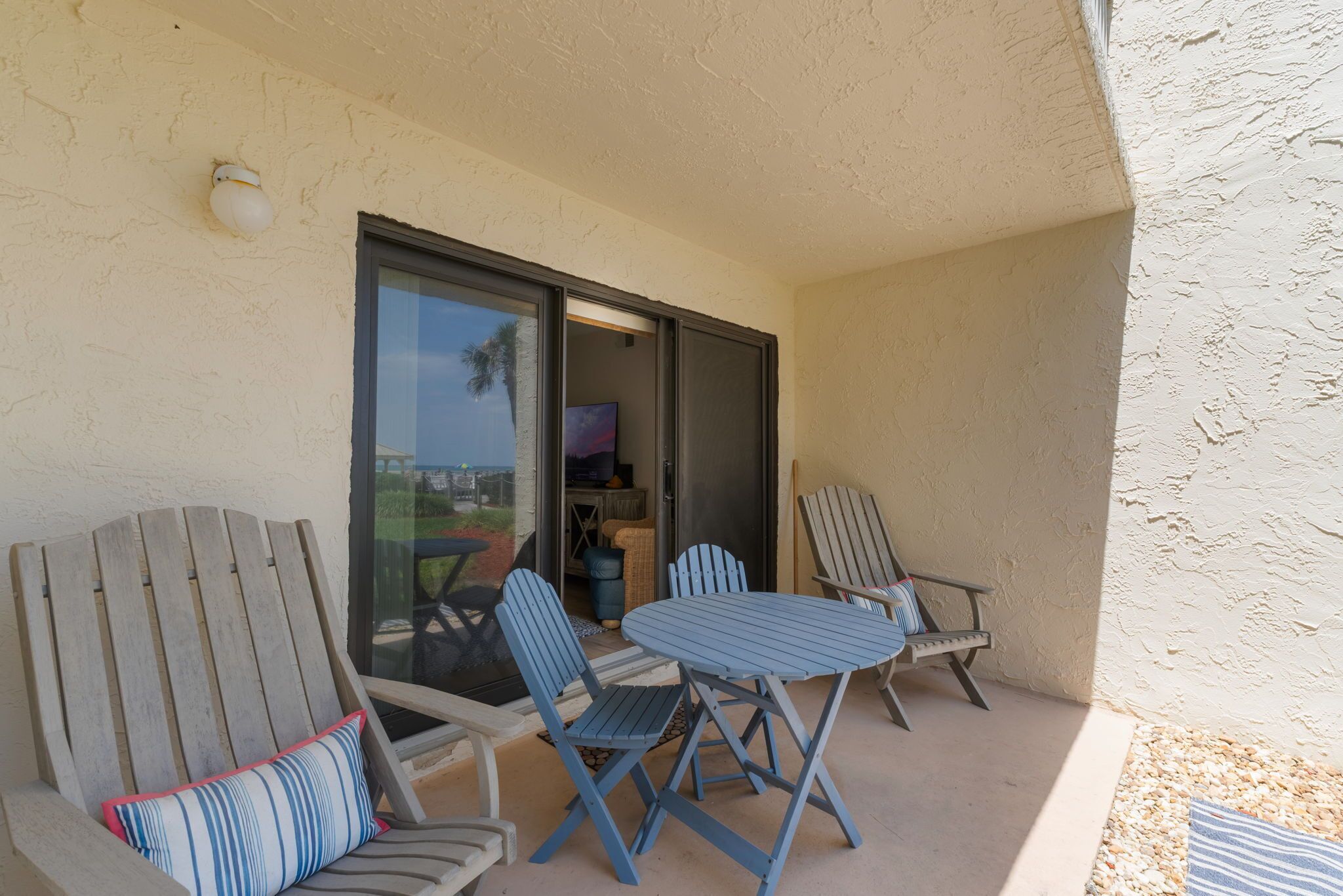 A balcony with two Adirondack chairs, a small table, and a sliding glass door leading to an interior space.