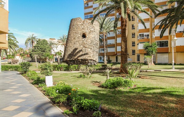 A courtyard with a stone tower, palm trees, and a tiled walkway. - Nice apartment in Algarrobo-Costa (Algarrobo-Costa)
