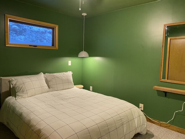 Une chambre à coucher avec un lit, un téléviseur fixé au mur, une lampe de chevet et une étagère en bois.