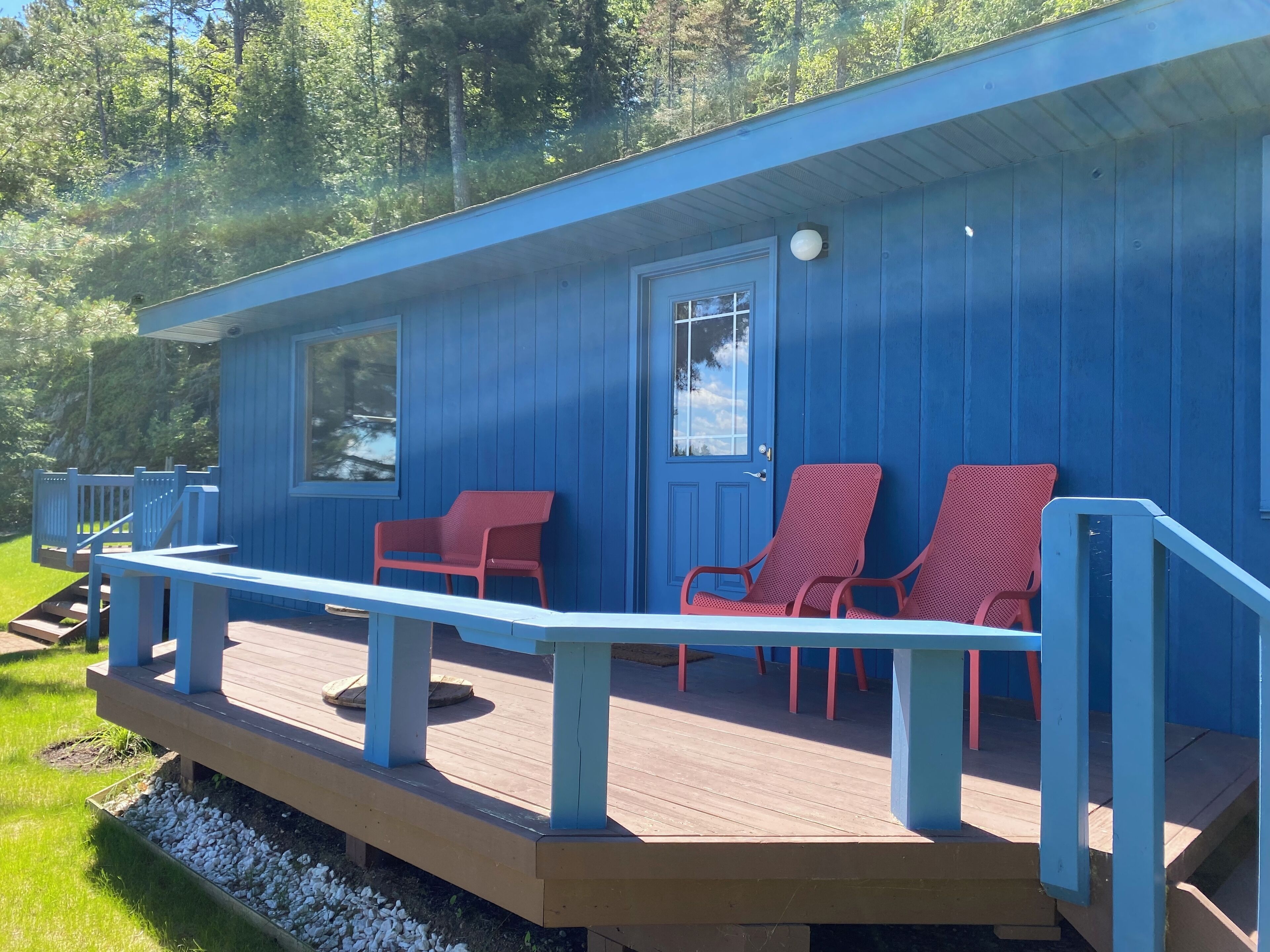 A blue cabin with a wooden deck, two red chairs, and a bench.